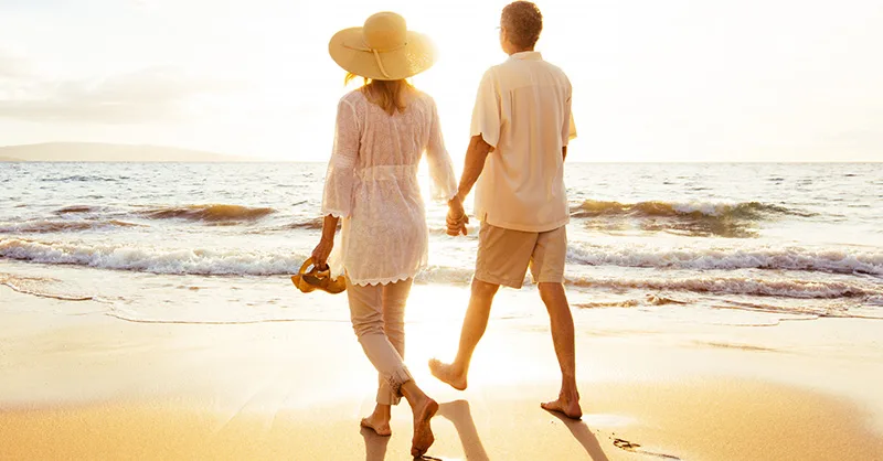 Image, photo d'un couple vu de dos, mains dans la main, marchant sur une plage au coucher du soleil.